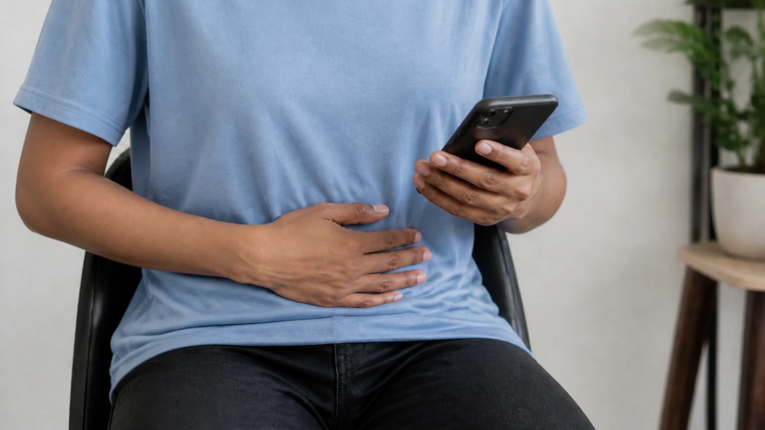 Person holding their lower abdomen while checking symptoms on a phone